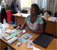 Woman seated at table, displaying various ICTs such as phones, CDs, and cassettes.